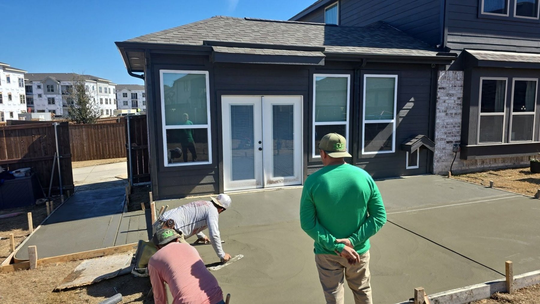 GreenGrows crew hand troweling a wet concrete patio slab in a DFW backyard